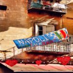 A Napoli il calcio fa parte della vita di tutti i giorni. Su un vecchio palazzo c’è uno striscione per festeggiare lo scudetto del Napoli. Intorno ci sono i balconi con i panni stesi e tanti cuori con i messaggi dei tifosi.